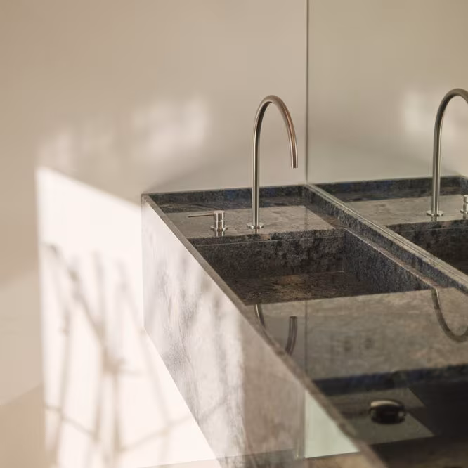 Dark stone double sink with stainless steel faucets at ÁBATON's Casa Brisa, featuring leaf-shaped shadows