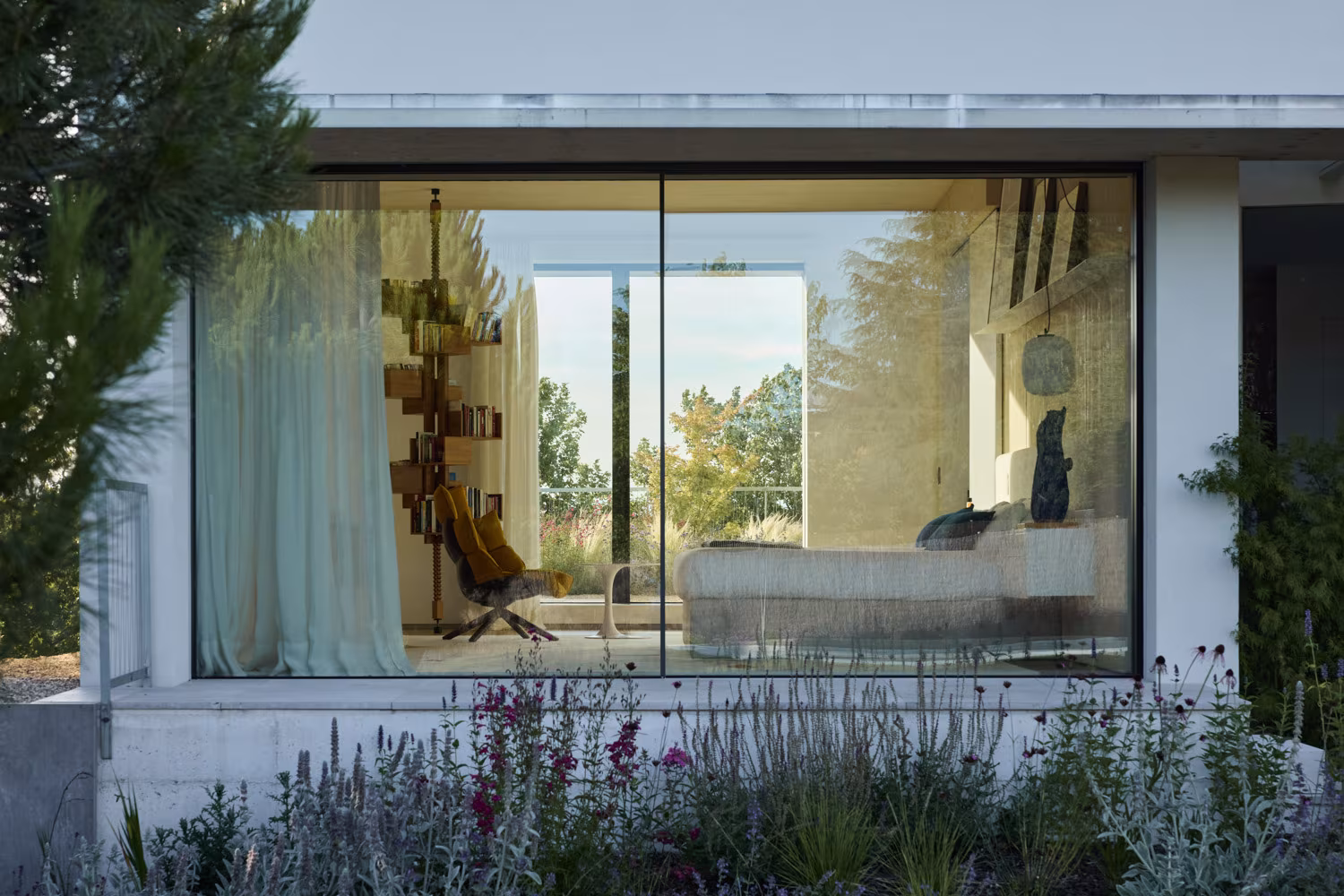 Large Casa Brisa window framing a bedroom with curtains, set among lavender and grasses