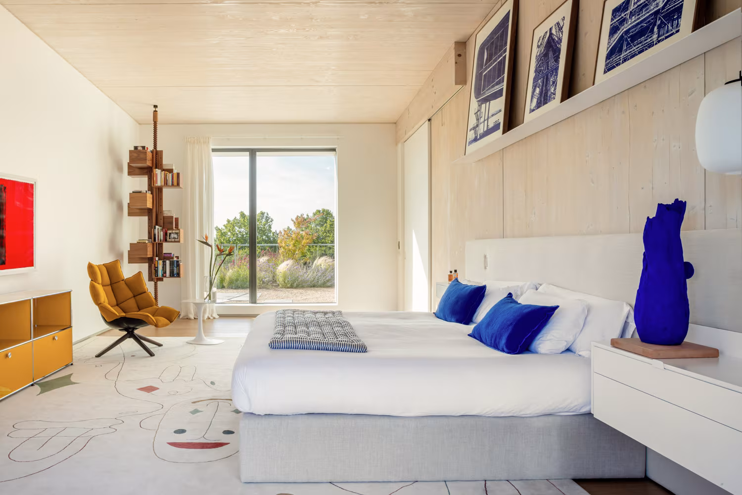Estantería vertical de madera junto a una silla de diseño en un dormitorio luminoso