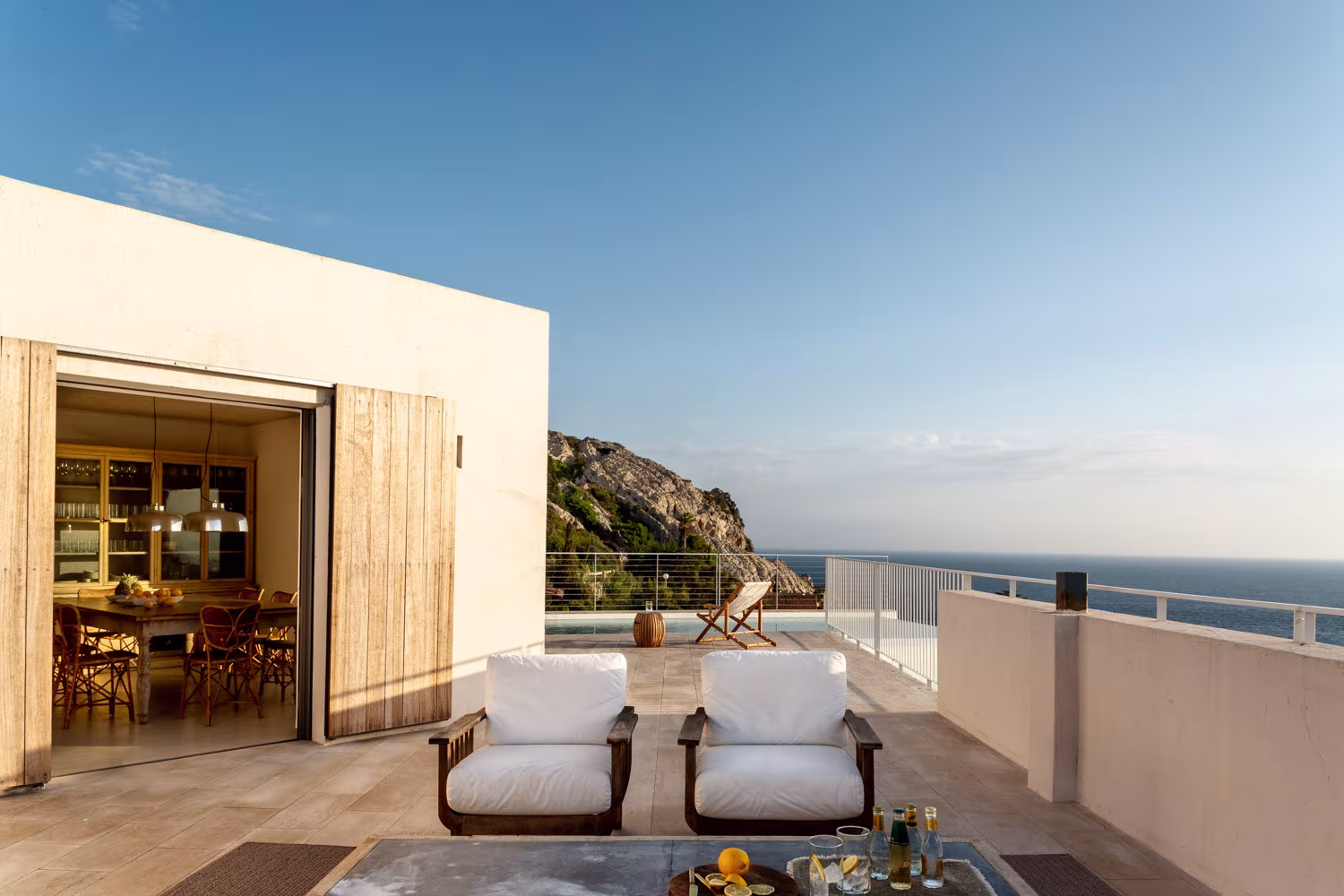Terraza mediterránea con vistas al mar y sillones de madera con cojines blancos