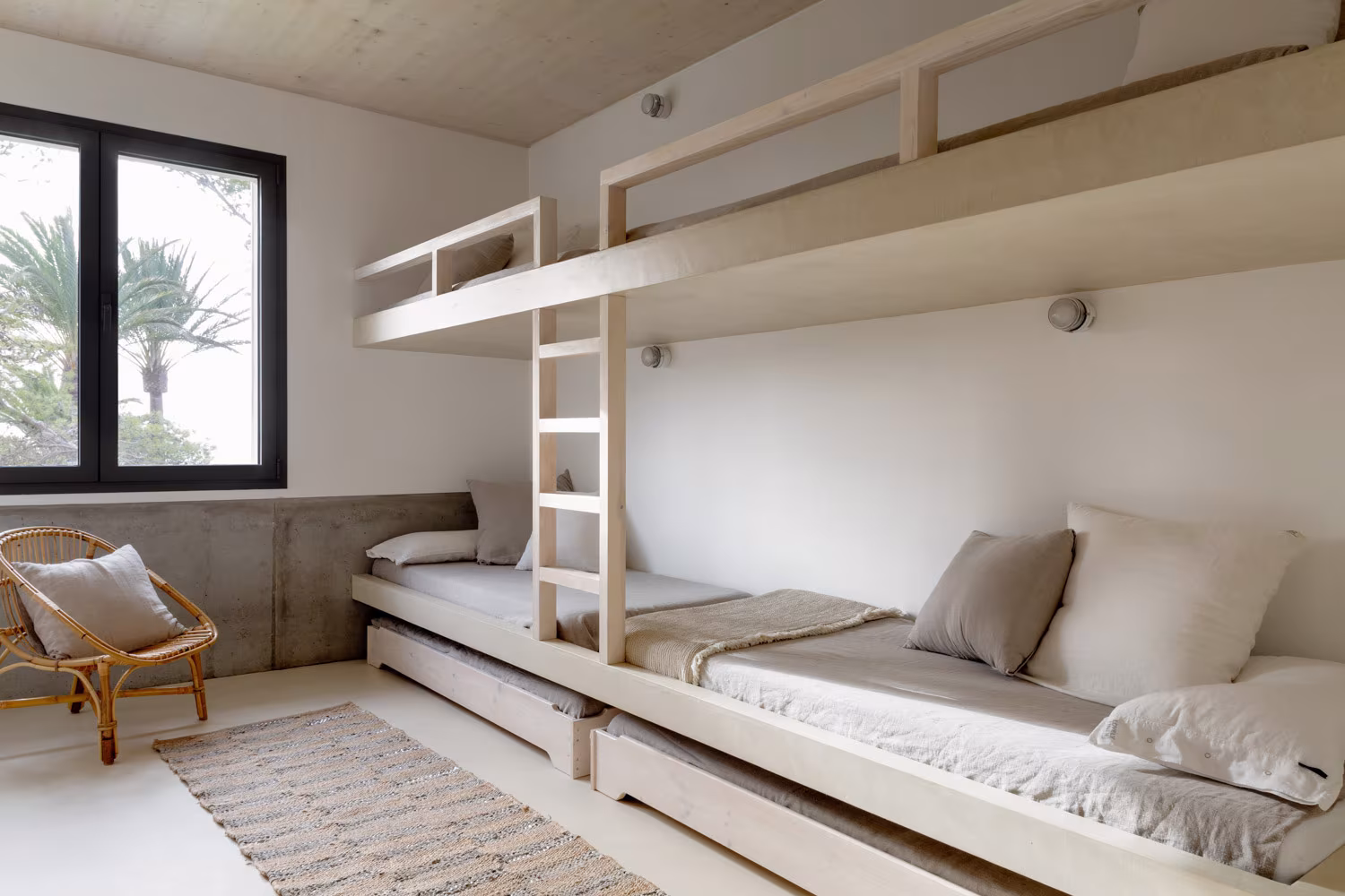 Dormitorio infantil mediterráneo con literas de obra beige y ventana negra con vistas a palmeras