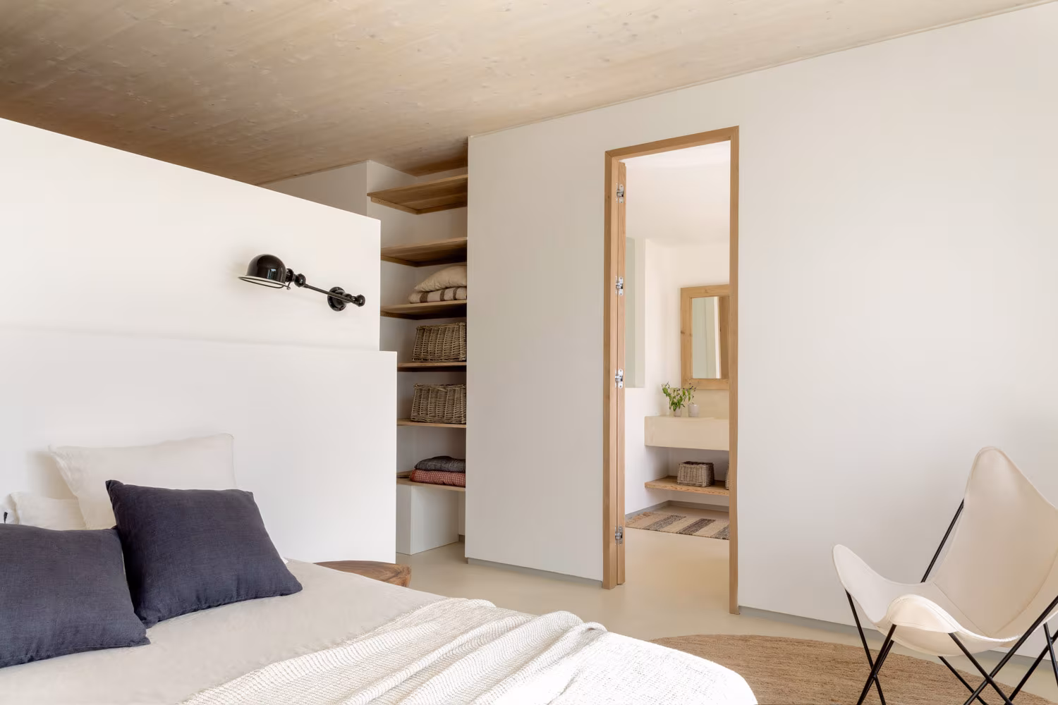 Dormitorio cálido con baño en suite, techo de madera clara y estanterías con cestas de fibra