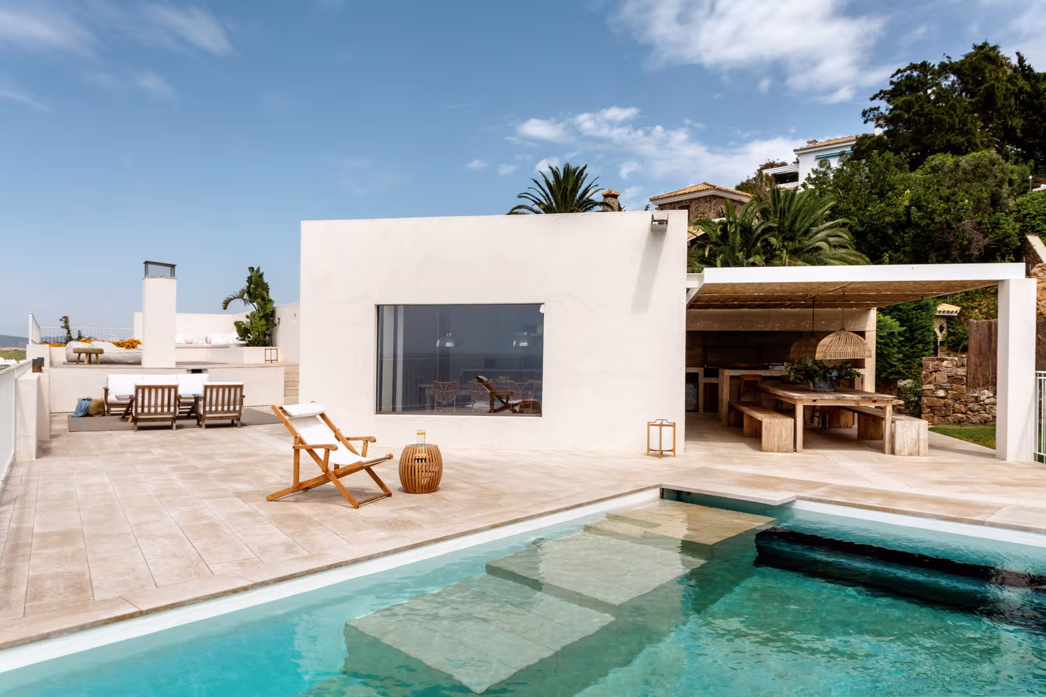 Terraza mediterránea con piscina escalonada, zona chill-out de sillones blancos y pérgola de cañizo