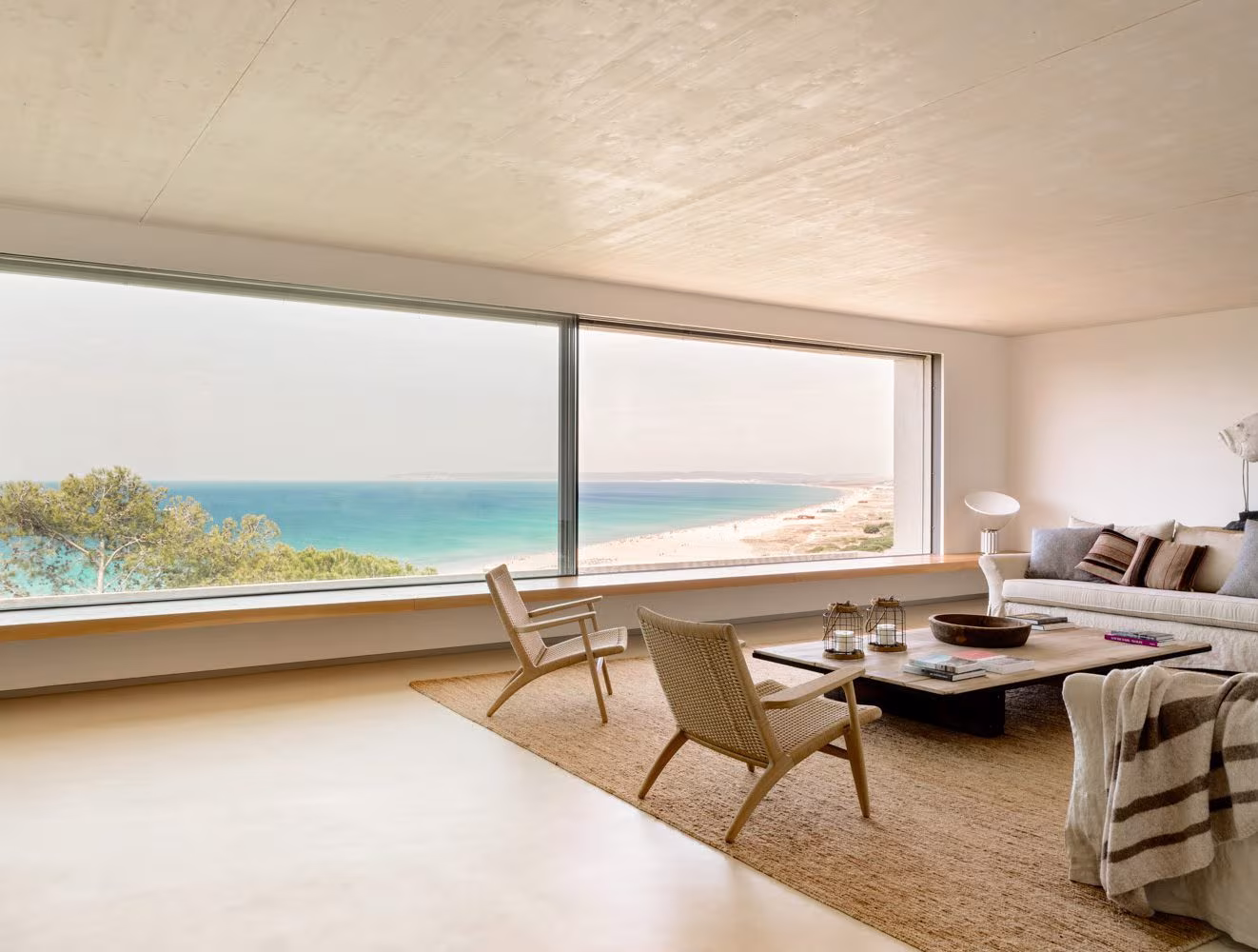Salón mediterráneo minimalista con ventanales panorámicos hacia el mar y la playa