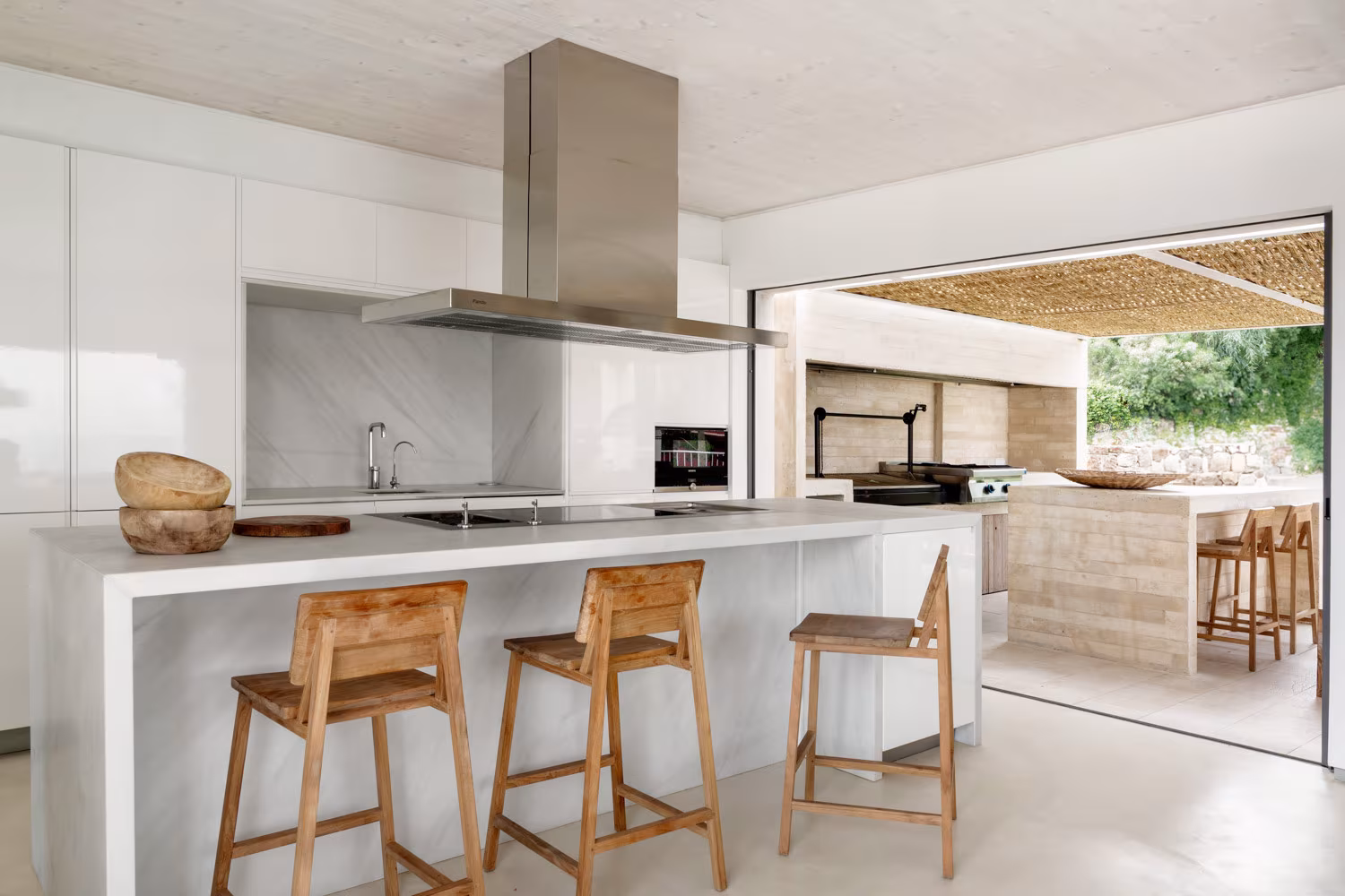 Cocina mediterránea con isla central de mármol blanco, taburetes rústicos y campana de acero