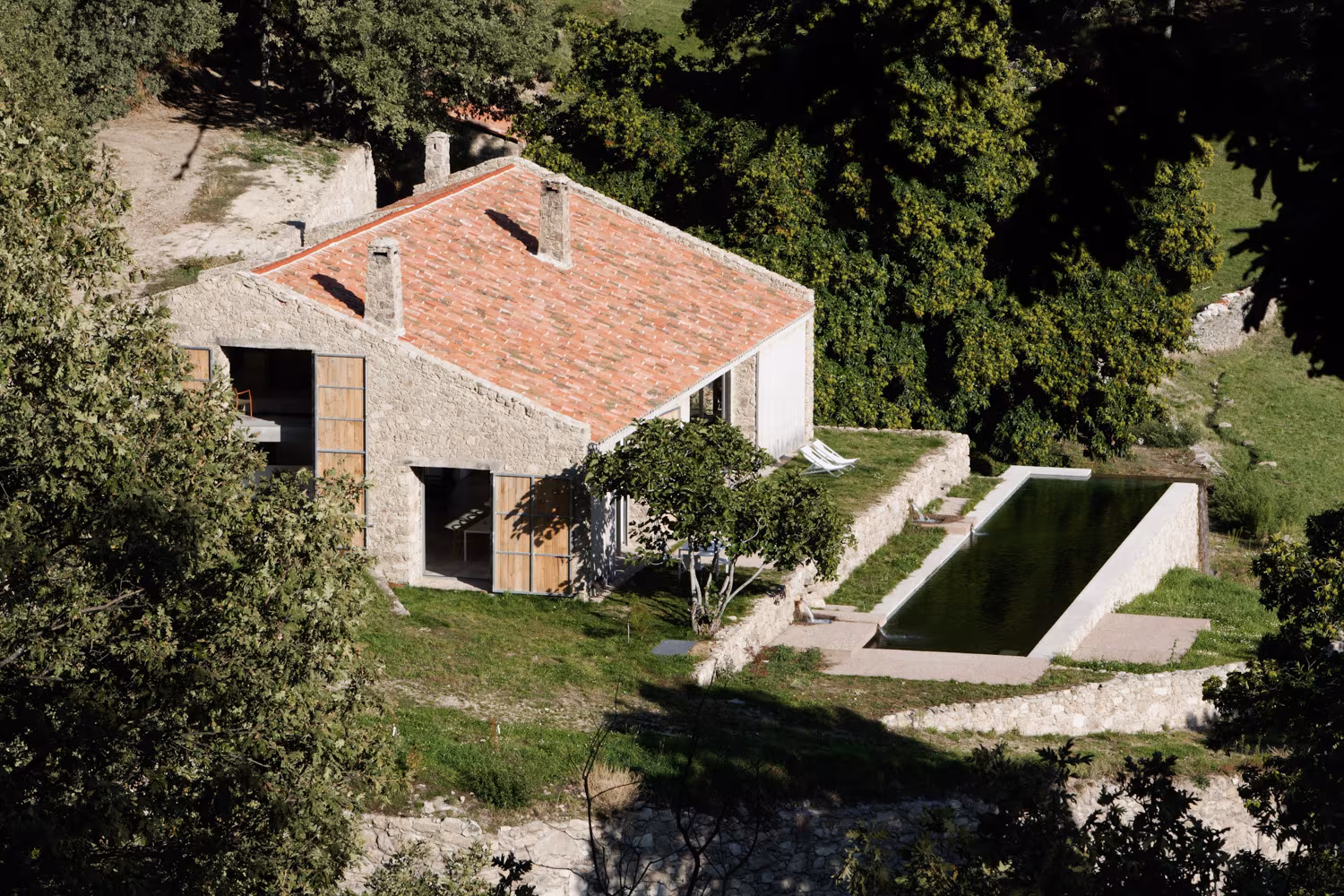 Casa rural de piedra con techo a dos aguas y piscina de agua natural en plena naturaleza. Diseño rústico y sostenible en un entorno verde y tranquilo