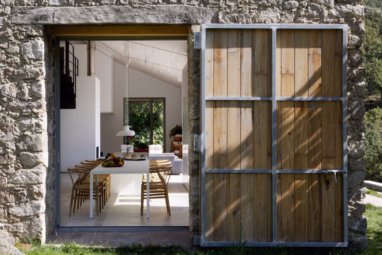 Entrada de la casa rural de piedra con puerta de madera rústica y amplio comedor abierto. Diseño minimalista y acogedor en plena naturaleza.