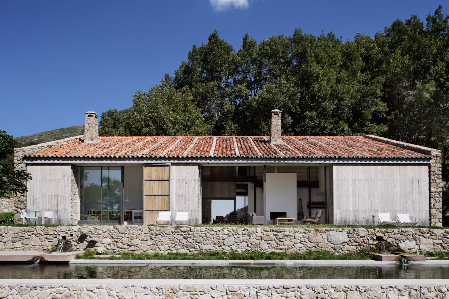 Finca rural de piedra y diseño moderno con tejado de tejas, grandes ventanales y piscina