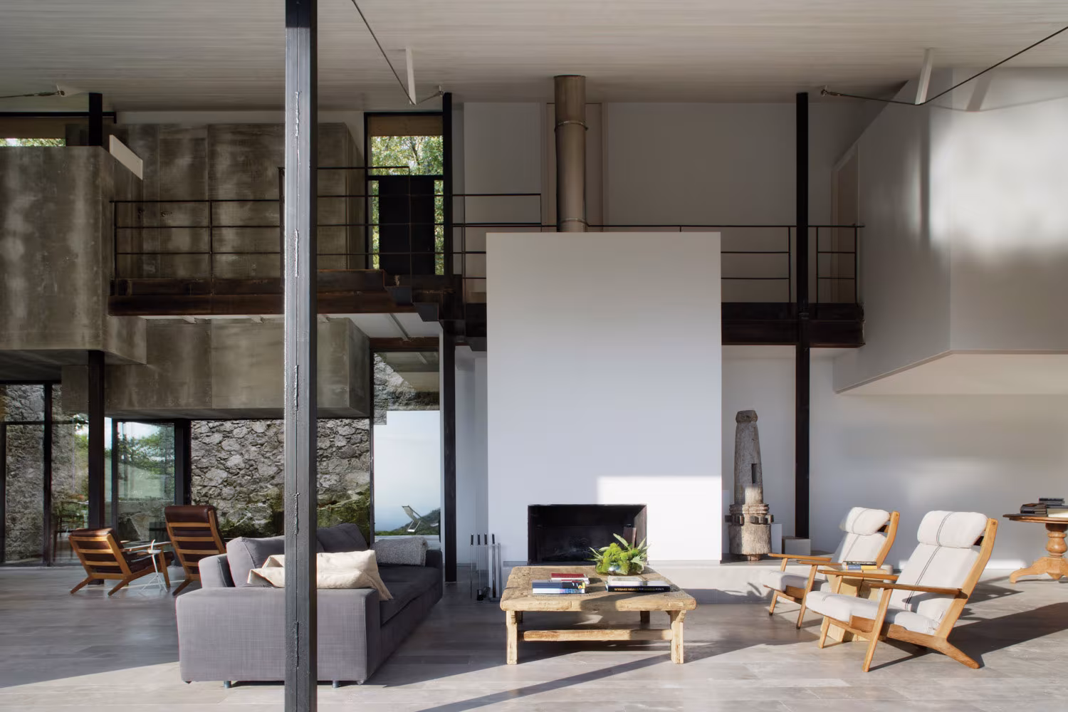 Salón de doble altura en hormigón, acero y piedra, con chimenea minimalista en pared blanca