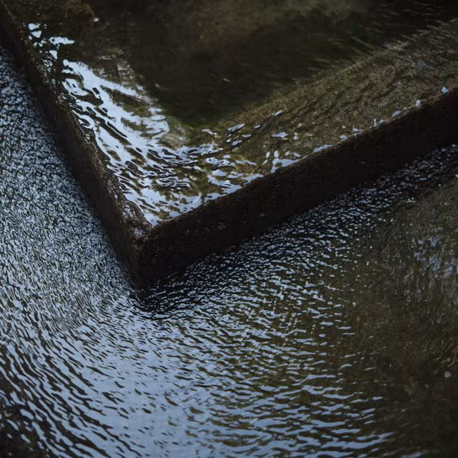 Water spilling over the corner of a dark stone fountain at ÁBATON's estate in Extremadura