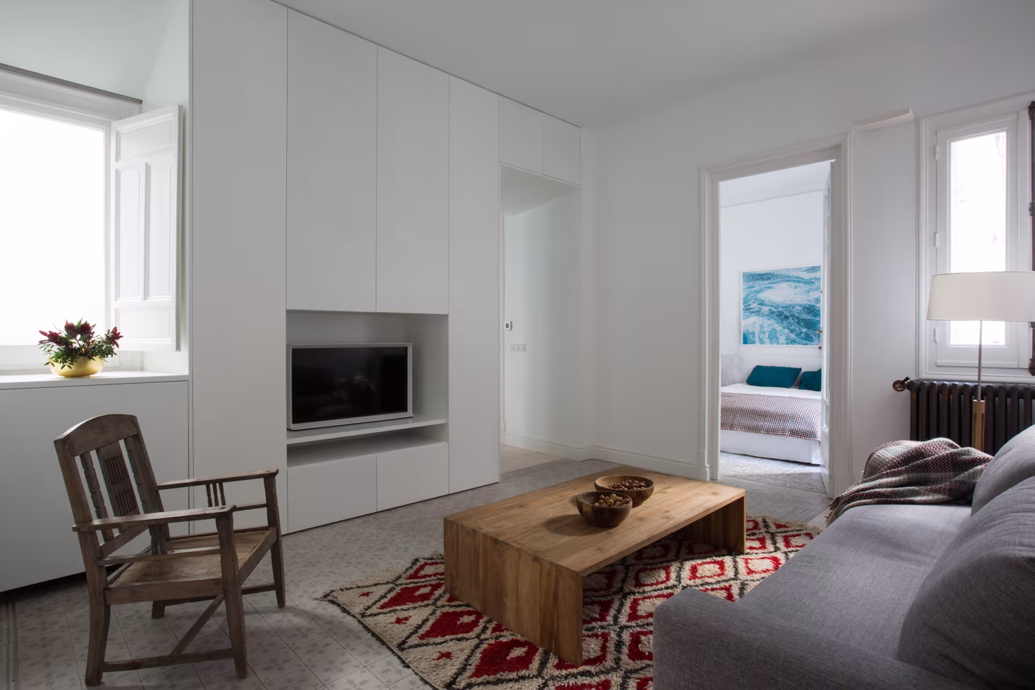 Sala de estar con mueble blanco empotrado, sofá gris y alfombra roja en la Reforma Integral en Sagasta I