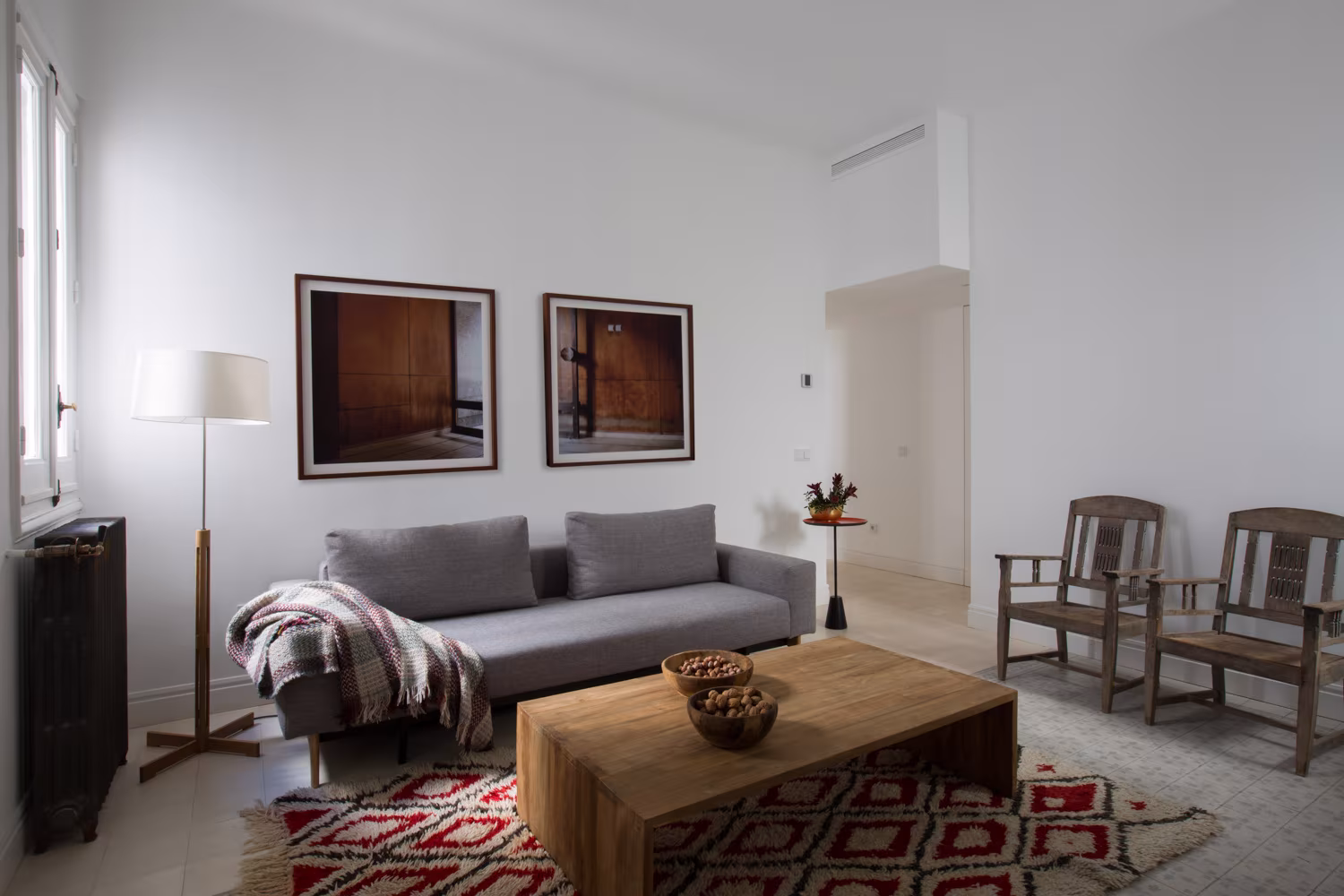 Salón con sofá gris, alfombra étnica, mesa de centro de madera rústica, lámpara de pie y sillas vintage en ambiente minimalista