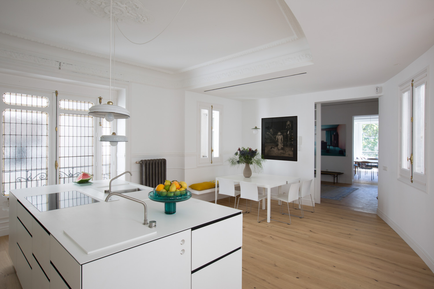 ABATON-reforma-integral-en-sagasta-19 Cocina minimalista blanca con isla central y grifería moderna, comedor con mesa rectangular, sillas blancas y suelo de madera clara