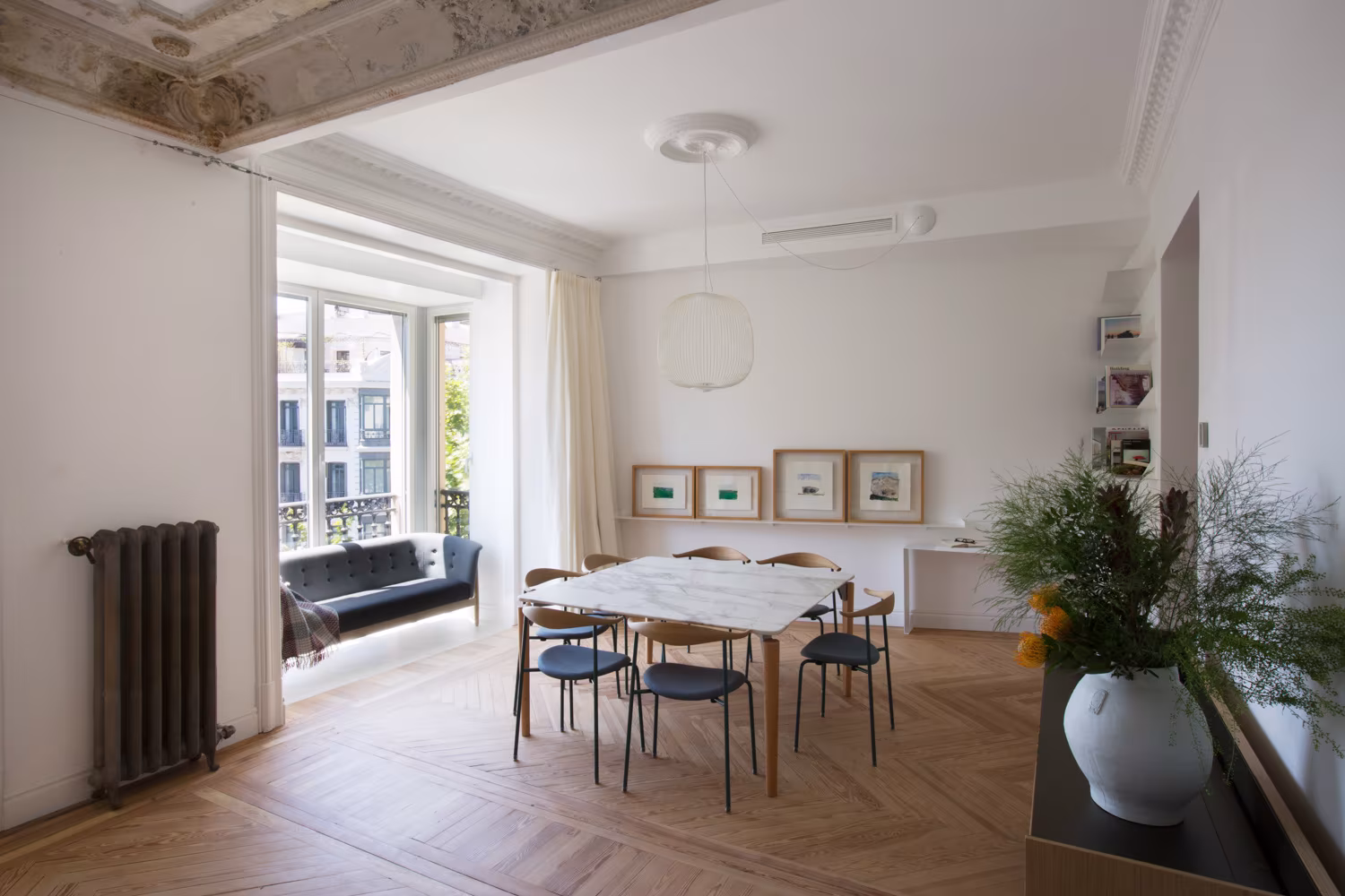 Comedor luminoso con mesa de mármol, sillas de diseño moderno, suelo de madera en espiga y molduras decorativas en el techo