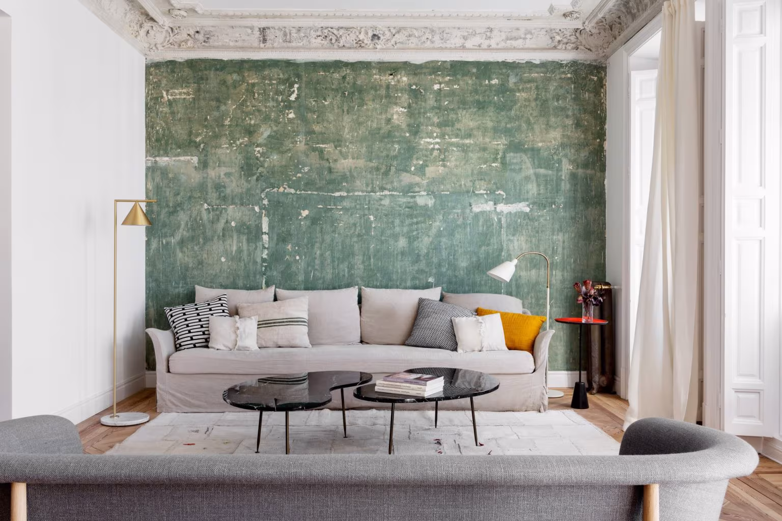 Salón con dos sofás grises de diferentes estilo, techo con molduras decorativas, pared verde desgastada y decoración contemporánea minimalista