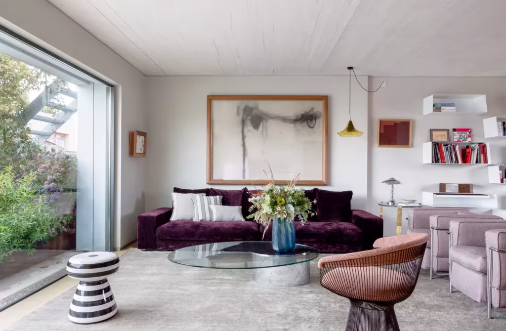 Salón contemporáneo con mesa de centro de cristal y sofá morado frente a las vistas del jardín