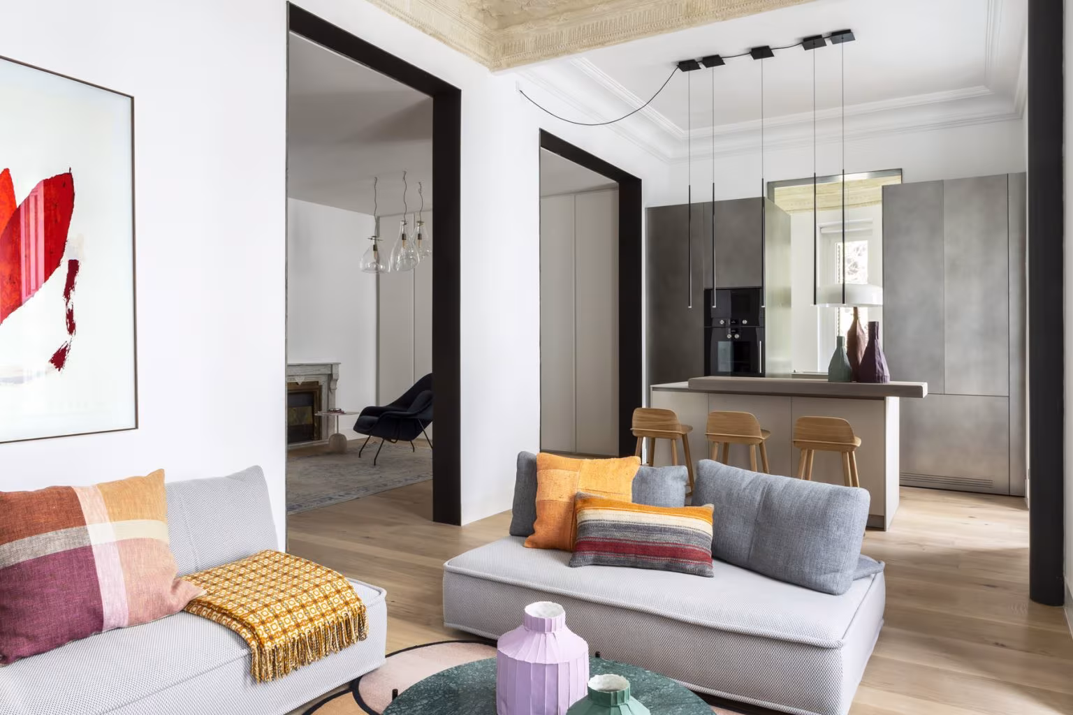 Salón y comedor de la reforma integral en Almagro, con sofá, obra gráfica y cocina al fondo bajo techo con molduras