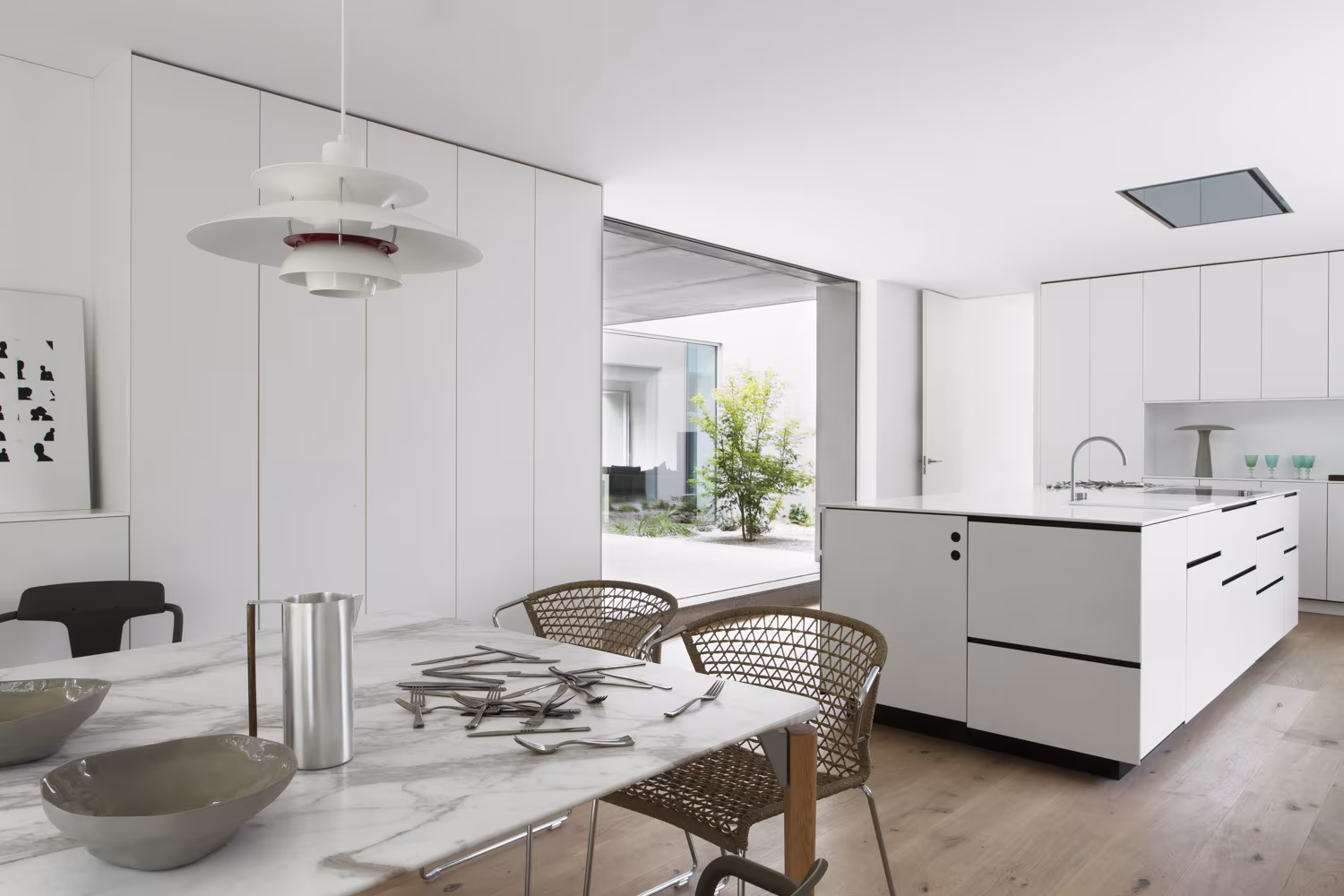 Comedor y cocina de Casa L con mesa de mármol, lámparas blancas y muebles de cocina empotrados