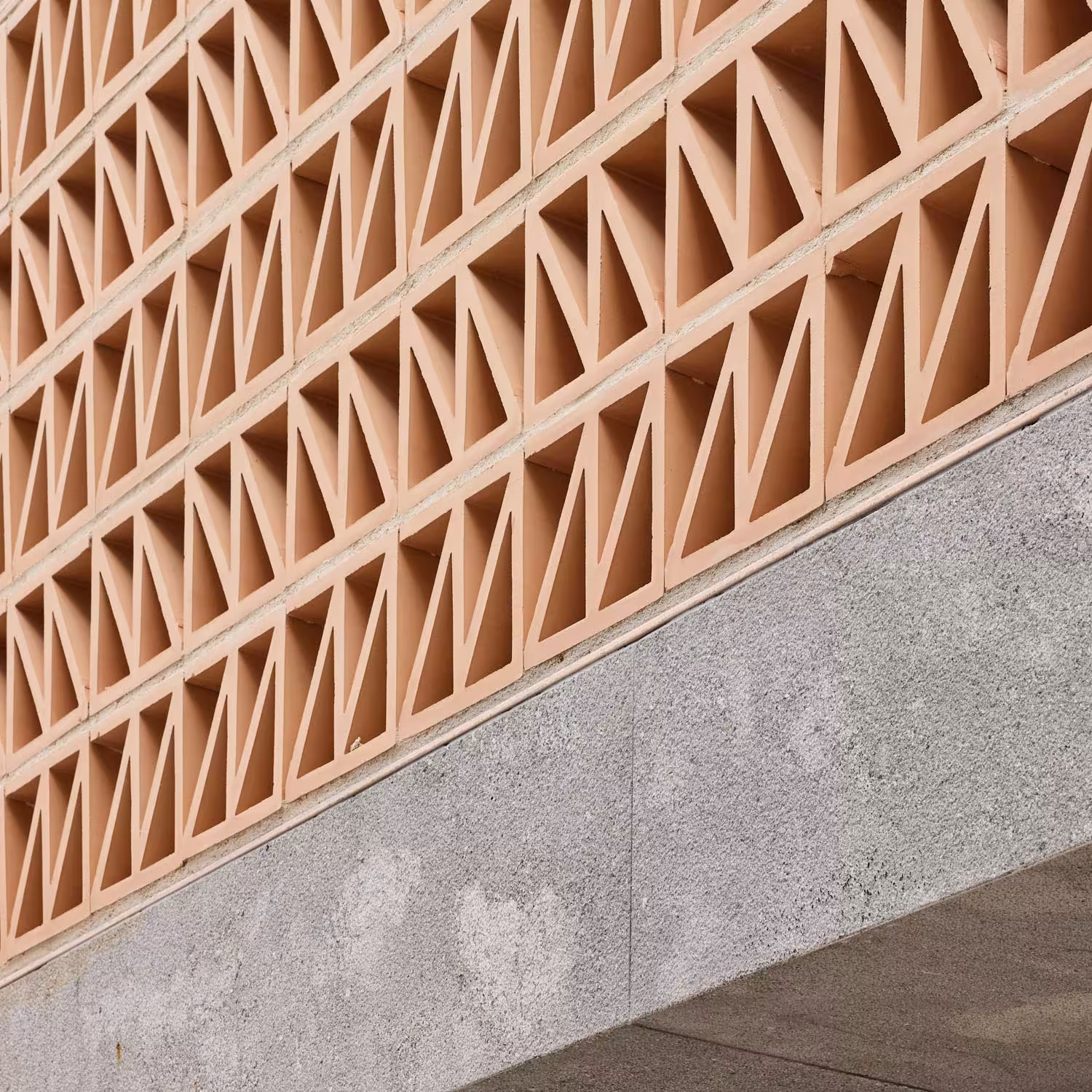 Celosía de ladrillo cerámico con huecos triangulares sobre un muro de hormigón visto