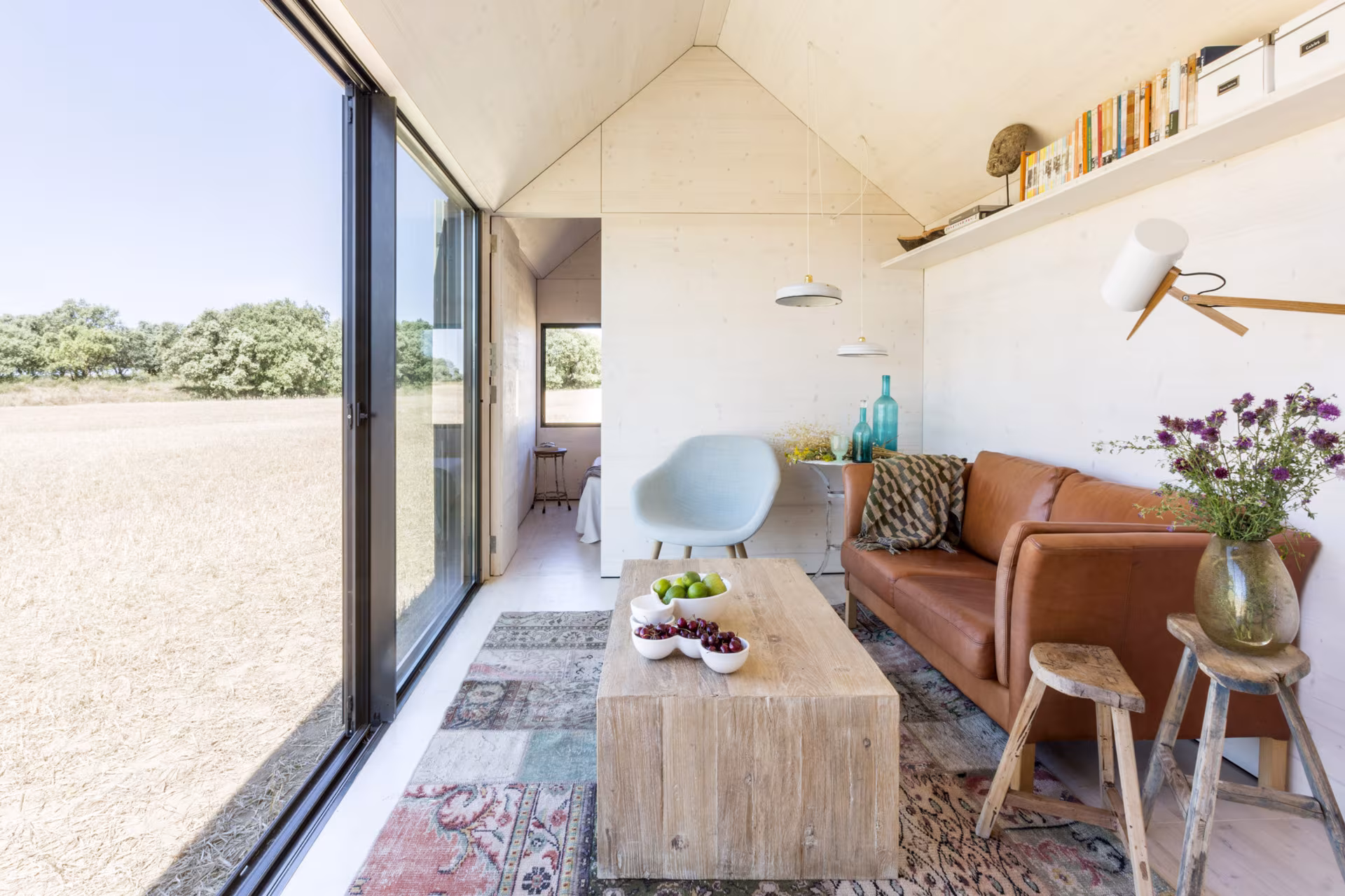 Interior de la casa transportable ÁPH80 con sofá de cuero, mesa de roble y una gran ventana corrida al campo