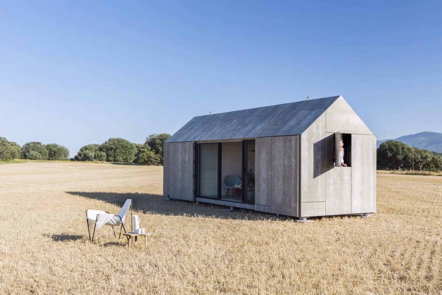 Casa transportable ÁPH80 en el campo con una silla blanca delante y la cubierta a dos aguas de hormigón gris