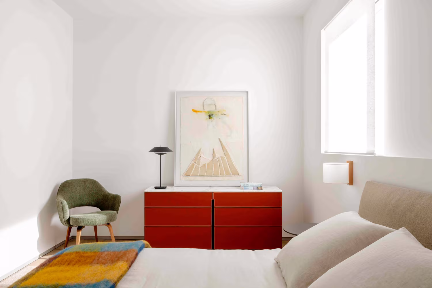 Dormitorio del ático sobre El Parque del Retiro con cómoda roja, sillón verde y manta de colores