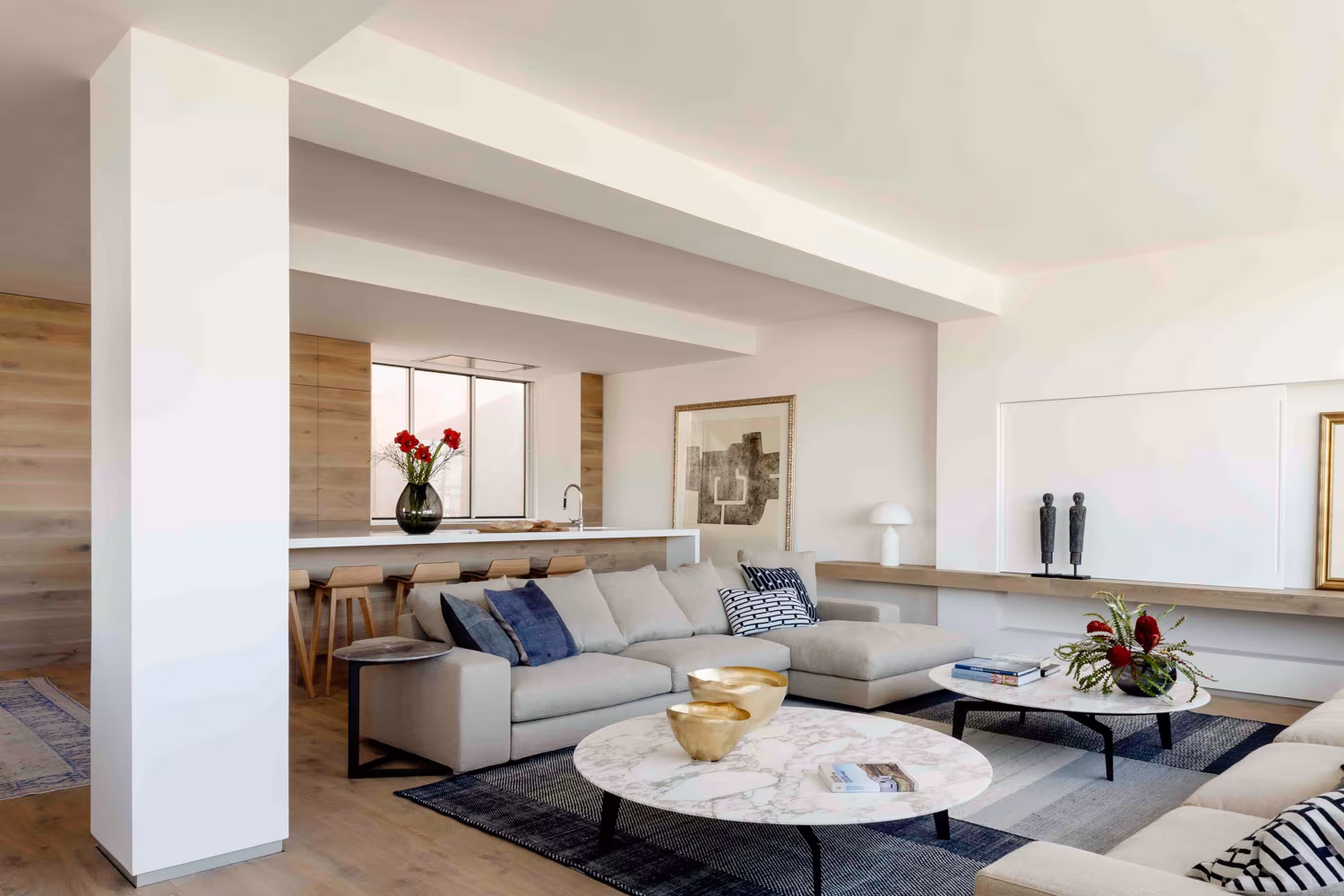 Salón con pilar blanco, cocina abierta, mesas de mármol y sofá beige, en el Ático sobre el Parque del Retiro de Ábaton