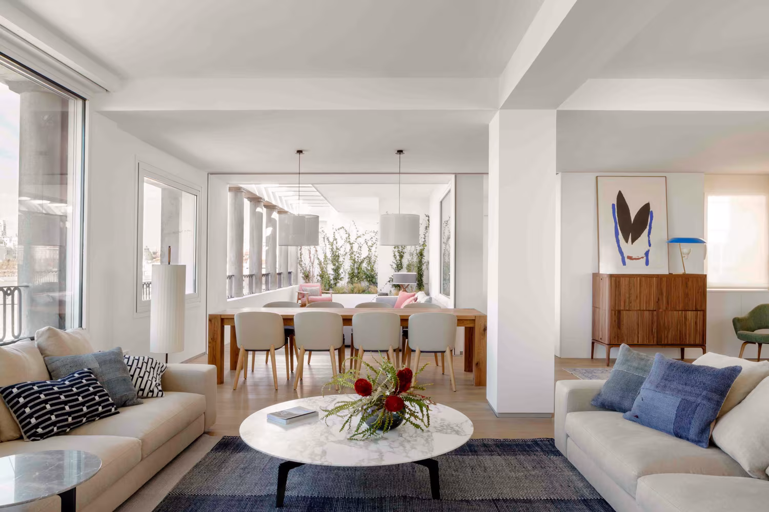 Continuous living and dining area with sofas, round marble table and a dining table beyond at the Retiro penthouse