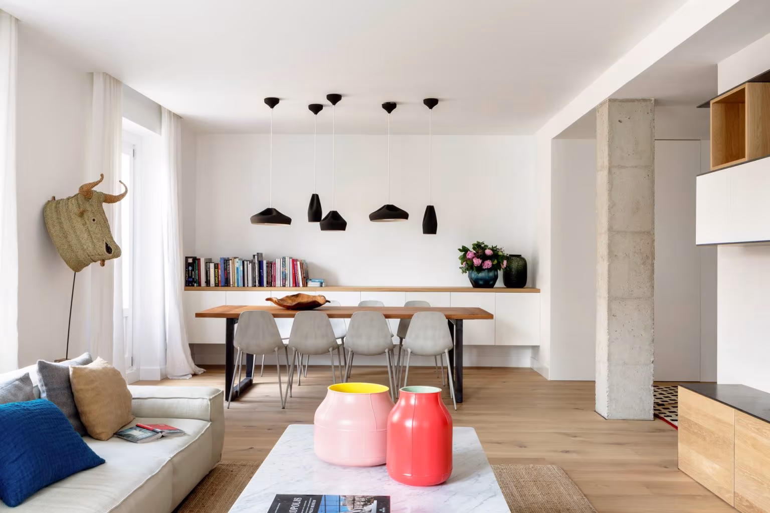 Comedor y salón abiertos con pilar de hormigón visto y estantes de roble en el piso de Casa Ayala II, Madrid
