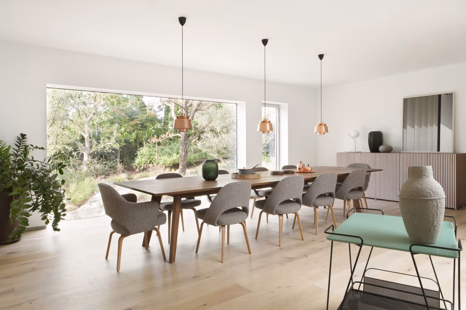 Comedor con mesa de madera, sillas tapizadas y lámparas de cobre ante un ventanal al jardín en Casa L