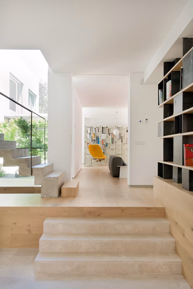 Pasillo de Casa L con escalones de madera clara, librería oscura y jardín al fondo en una reforma de Ábaton