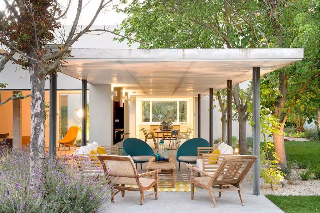 Concrete porch with timber armchairs and lounge seating in front of a lit living room, House L by Ábaton, Madrid