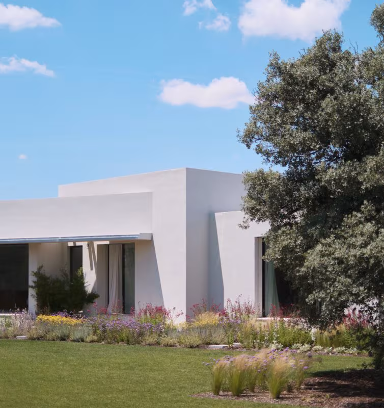 Single-storey white house by ÁBATON with a garden of grasses and flowers beside a large holm oak