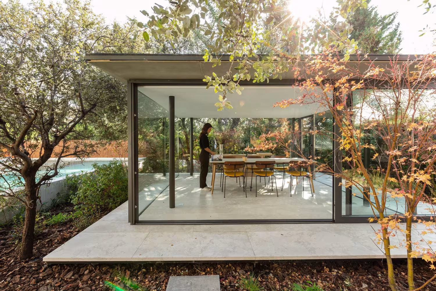 ABATON-pabellon-del-jardin-10 Glazed pergola with slim frames seen from the garden, a figure standing beside the dining table