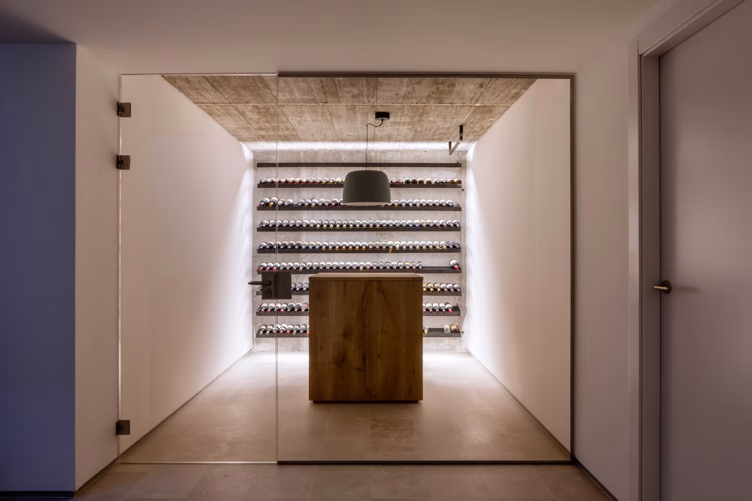 Bodega acristalada con botelleros iluminados y una isla de roble en un pasillo de la casa de las luces