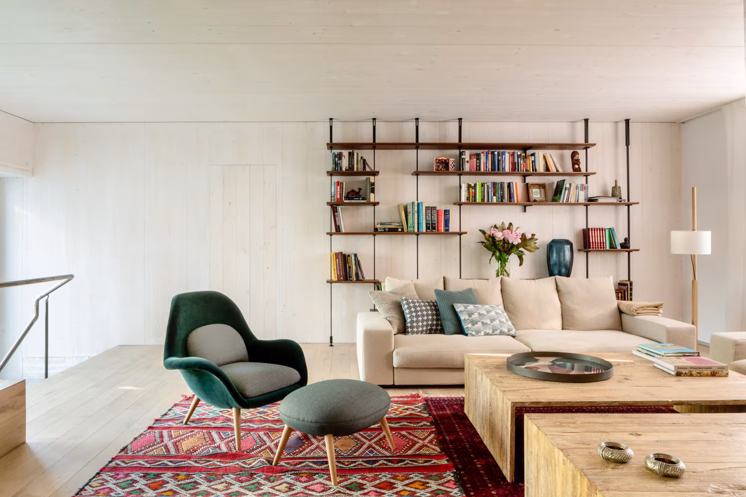 Salón con librería metálica, butaca verde, mesa de madera y alfombra kilim en la casa de las luces