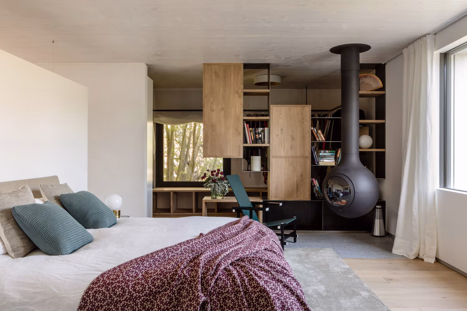 Dormitorio con chimenea colgante negra y mueble de roble al fondo, en la casa de las luces de Ábaton