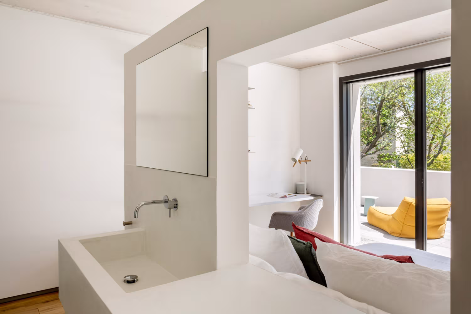Lavabo de pared blanca con espejo abierto a un dormitorio y a una terraza, en la casa de las luces de Ábaton
