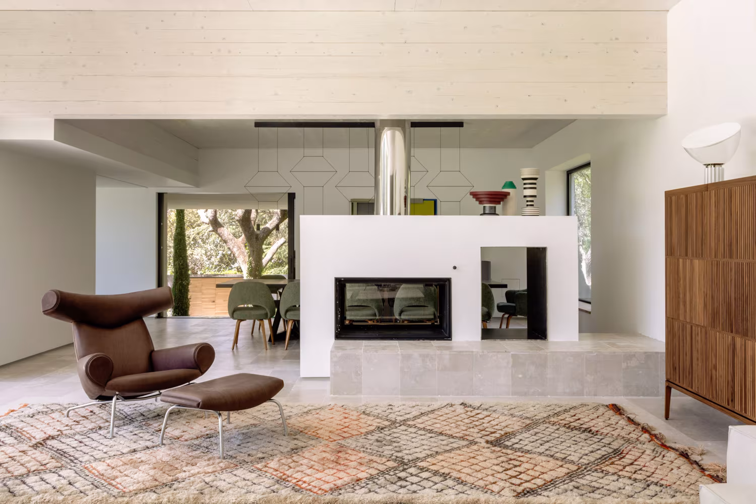 Salón con chimenea central de doble cara, butaca de cuero y alfombra de rombos en la casa de las luces de Ábaton