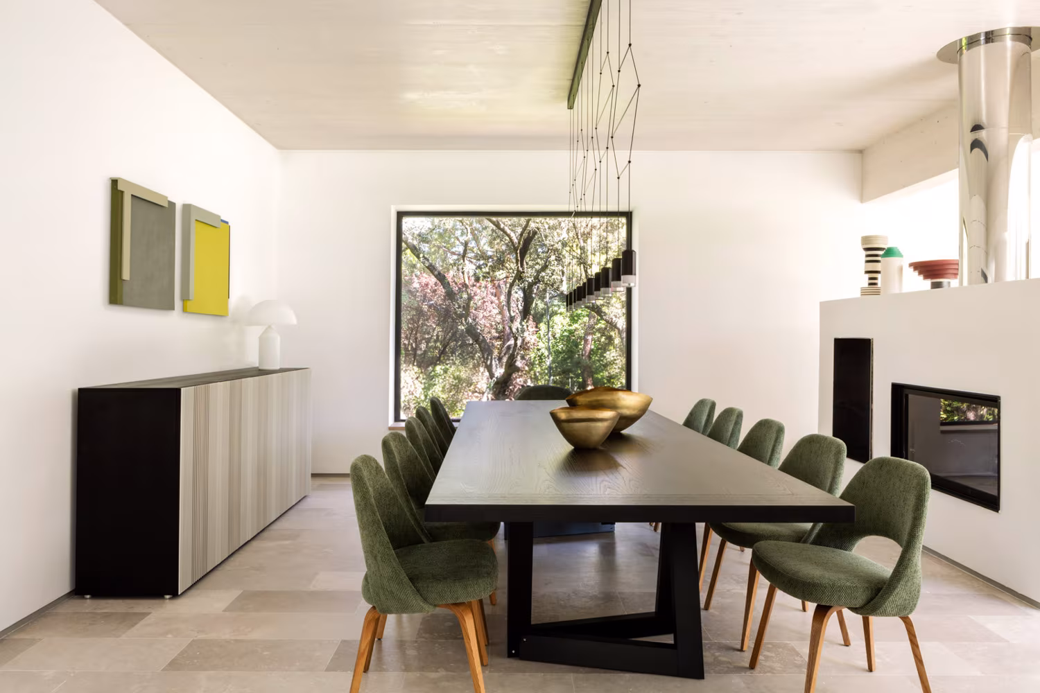 Comedor visto en perspectiva con mueble bajo gris, cuadros y chimenea al fondo en la casa de las luces