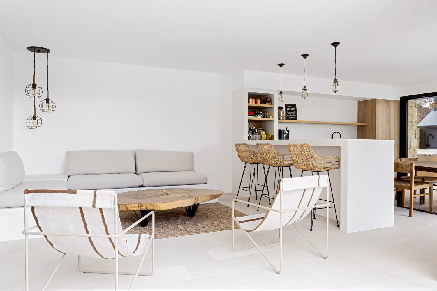 Open-plan living and kitchen area in white with light armchairs, timber coffee table and stools, Proyecto V-E