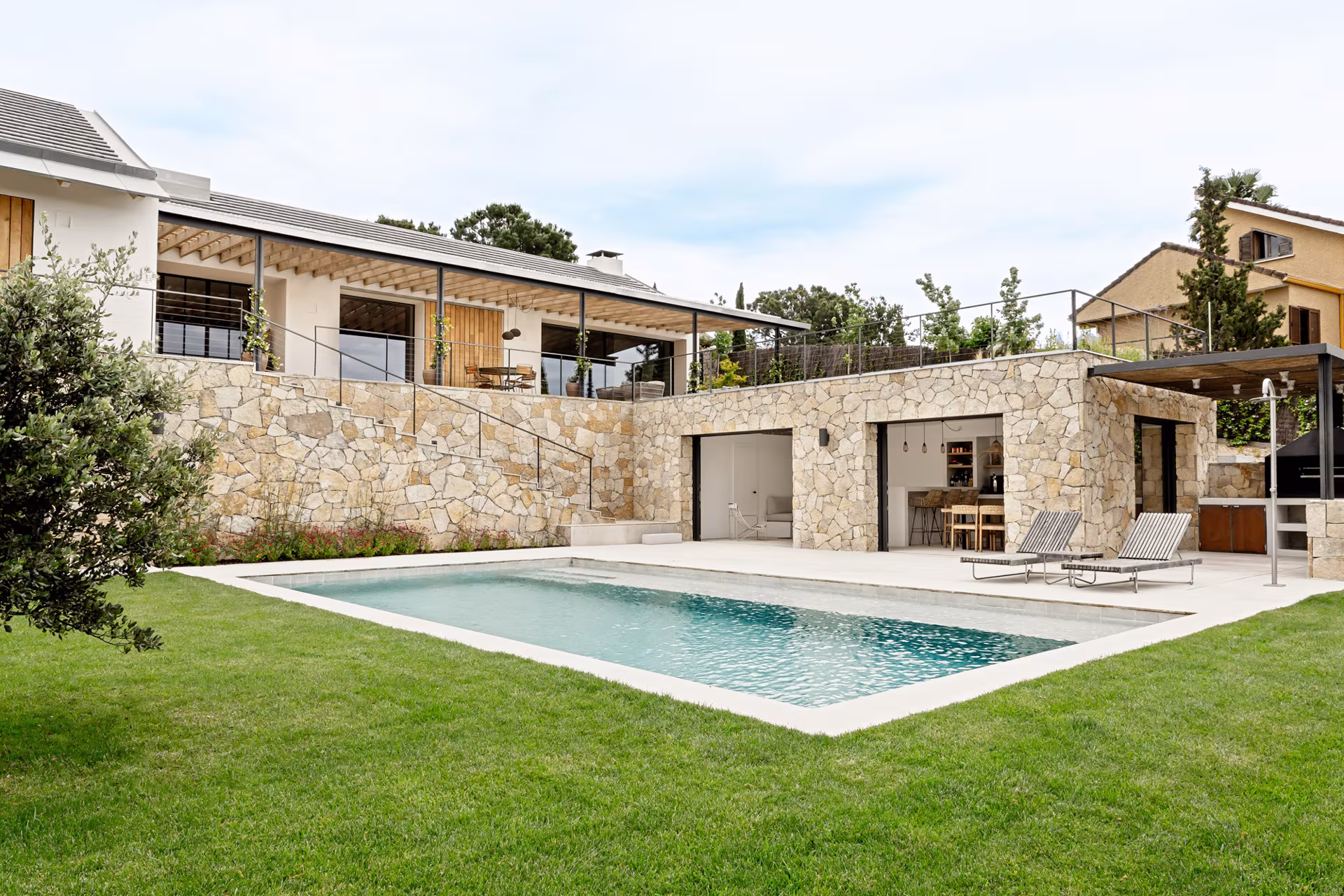View of Proyecto V-E by Ábaton from the garden, with pool, stone plinth and slate roofs