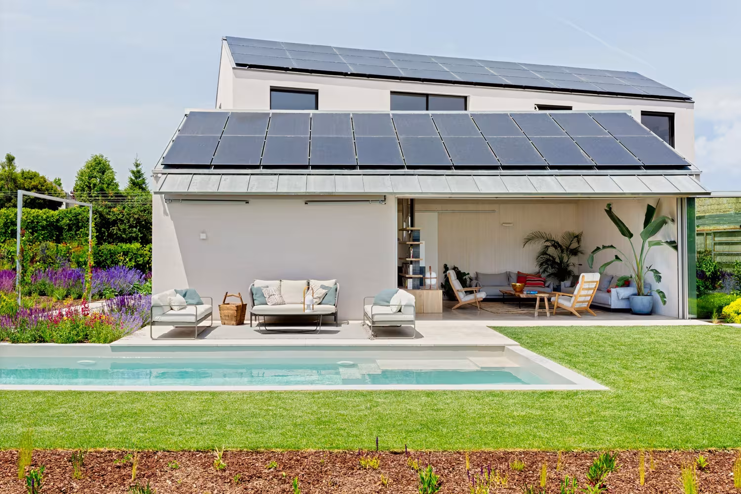 Rear façade of the Valladolid house with solar panels, an open porch and a pool surrounded by lawn