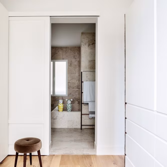 White sliding door open onto a stone bathroom with stool, Almagro refurbishment, Madrid