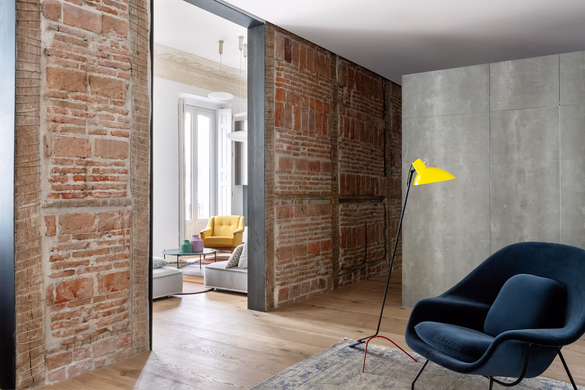 Reclaimed brick and concrete walls with a blue armchair and yellow lamp in Casa Ayala, an Ábaton refurbishment in Madrid
