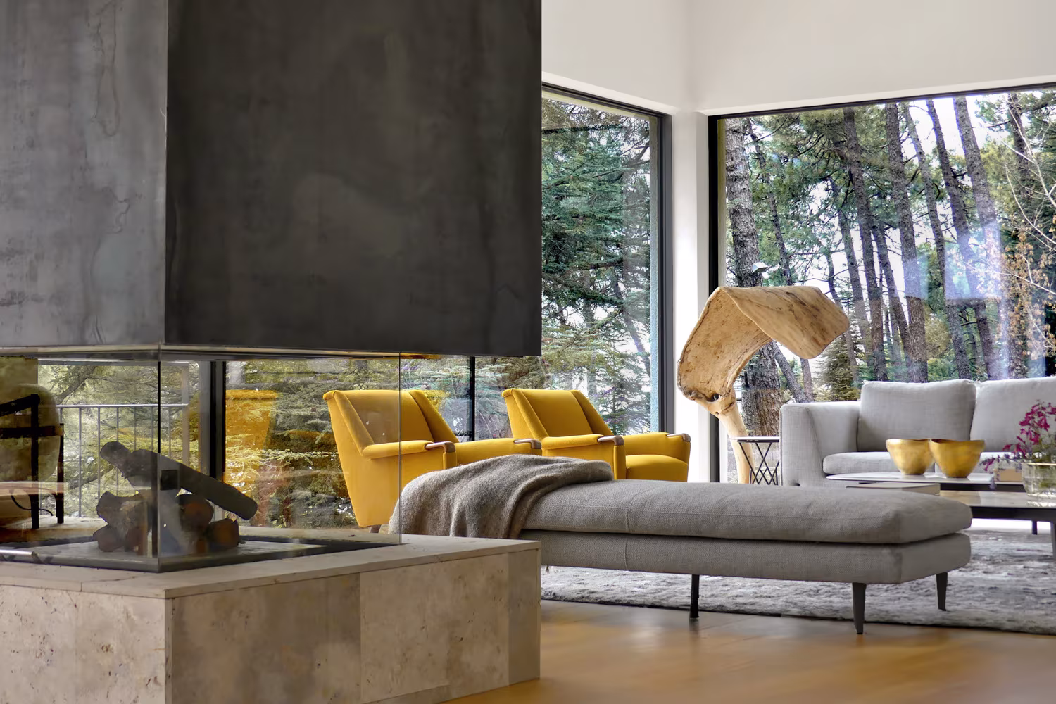 Salón moderno con chimenea central, sillones amarillos y vistas al bosque a través de ventanales panorámicos