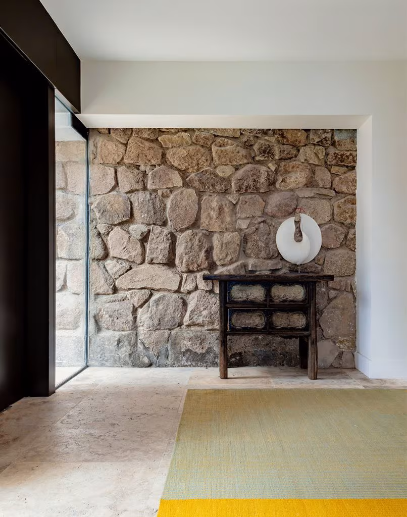 Pared de piedra rústica con consola vintage y escultura decorativa en entrada de casa moderna
