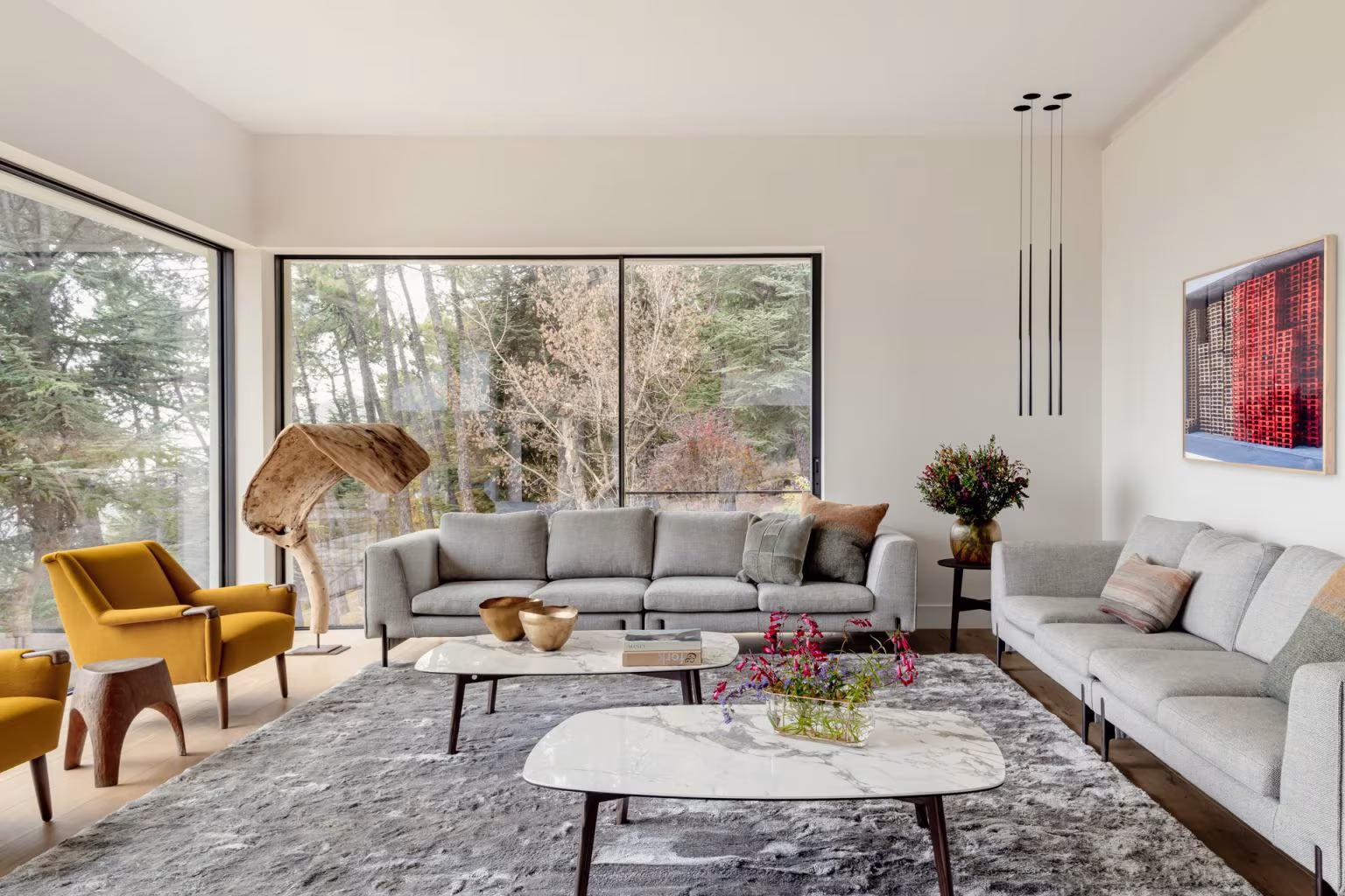 Salón contemporáneo con ventanales de aluminio, sofás grises modulares, sillones mostaza y mesa de centro de mármol