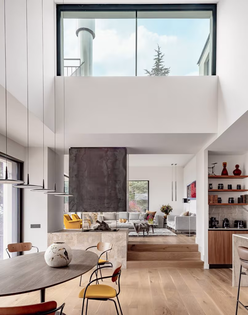 Salón, comedor y cocina de diseño moderno con grandes ventanales, sofá gris, sillón amarillo, mesa redonda de madera y estantería abierta