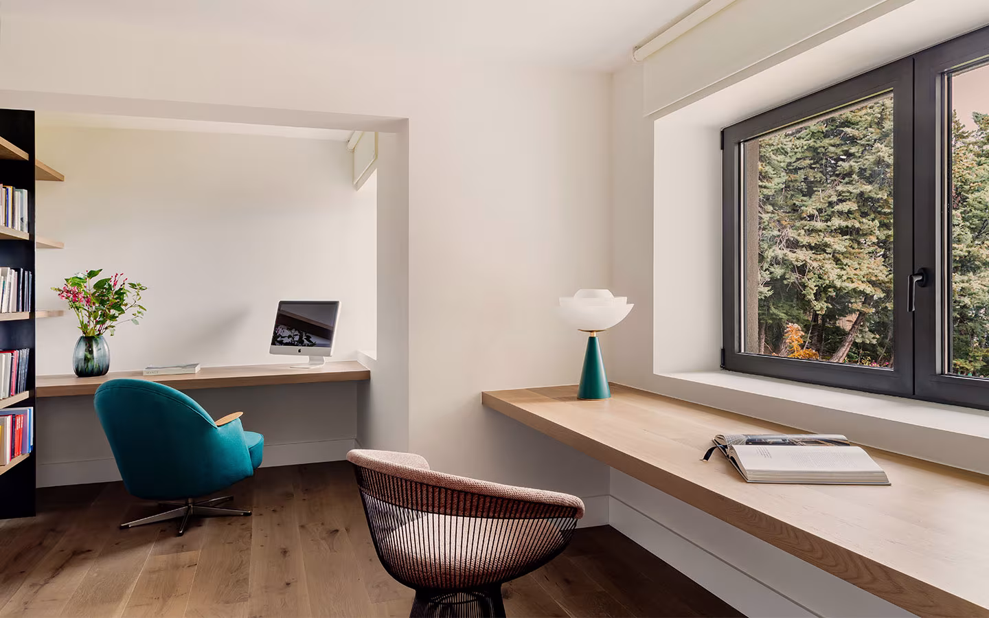 Zona de estudio minimalista con doble escritorio de madera, dos sillas y ventana con vistas a zona boscosa.